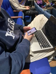 a person using a cell phone while sitting in front of a laptop on a blue chair