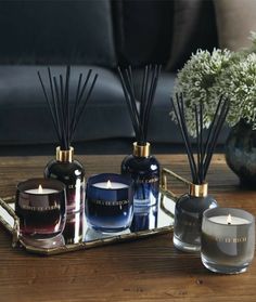 candles and vases on a table with flowers in the background, including an air freshener