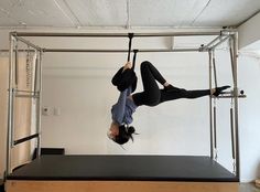 a woman hanging upside down on a bar in a room with white walls and black flooring