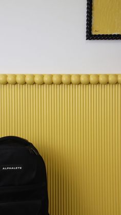 a black backpack sitting next to a yellow wall