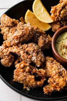 fried chicken and dipping sauce on a black plate with lemon wedges next to it