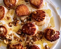 a white plate topped with scallops covered in sauce and nuts on top of a table