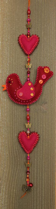 two red birds hanging from strings on a wooden wall next to a mirror with beaded trimmings