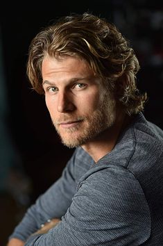 a man with long hair and a beard is looking at the camera while wearing a gray shirt