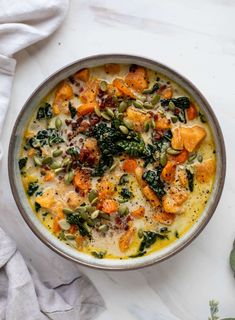 a bowl filled with soup and vegetables on top of a white table cloth next to a napkin