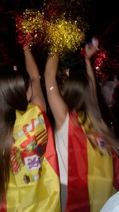 two girls in yellow and red dresses are holding their hands up with fireworks behind them