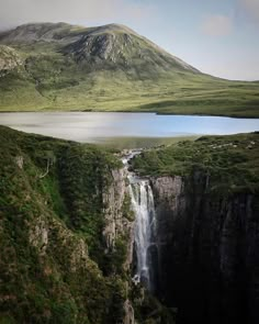 a waterfall in the middle of a large body of water surrounded by lush green hills