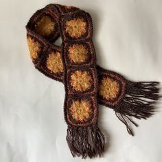 a crocheted scarf is laying on a white sheet with brown and yellow squares