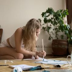 a woman is sitting on the floor drawing with a pencil and watercolors in front of her