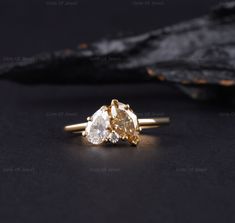 two pear shaped diamond engagement rings sitting on top of a black surface with gold band