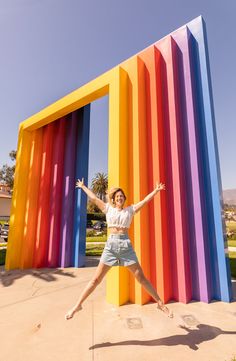 a woman standing in front of a rainbow colored structure with her arms outstretched and legs spread out