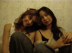 two young women sitting next to each other on the floor in front of a tiled wall