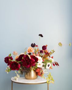 an instagram page with flowers in a gold vase on a white table and blue background