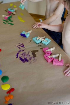 two children are playing with popsicle art on the table while one child is holding a toothbrush