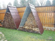 two large piles of firewood sit in the back yard next to a wooden fence