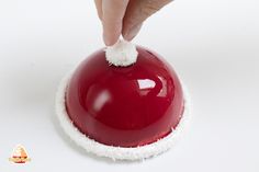 a hand is touching the top of a red object with white snow on it's edges