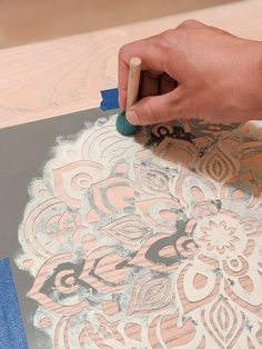 a person using a brush to paint an ornate design on a piece of paper with blue tape