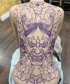 the back of a woman's body with tattoos on it and flowers around her neck