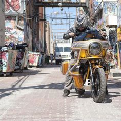 a man riding on the back of a yellow motorcycle down a street next to graffiti covered buildings