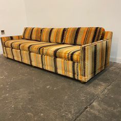 an orange and black striped couch sitting on top of a cement floor next to a white wall