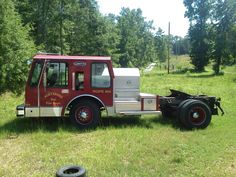 an old fire truck is parked in the middle of a grassy field with trees behind it