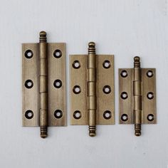 three brass plated door hinges on a white wall with screw holes in the middle