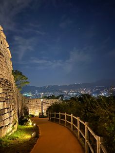 a path leading up to the top of a stone wall at night with lights on