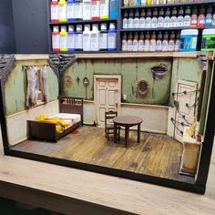 a doll house with furniture and paint on the walls, in front of a shelf full of bottles