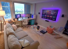 a living room filled with lots of furniture and two monitors on the wall above them