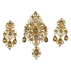 Museum-quality antique late 17th/early 18th century diamond and yellow gold Baroque "sequilé” earrings and pendant/brooch demi-parure, Portuguese, with hallmarks from the period and in the original case. This Georgian sequilé jewel from the first half of the 1700s features intricate filigree, pierced, and die-pressed gold work. It is closed-back set throughout with table-cut and rose-cut diamonds, notable for their almost crude simplicity. The pieces are richly adorned with chiseled and scallope Ornate Baroque Jewelry With Rose Cut Diamonds, 22k Gold Victorian Ceremonial Jewelry, Baroque Rose Cut Diamond Gold Jewelry, Baroque Gold Jewelry With Rose Cut Diamonds, Gold Baroque Jewelry With Rose Cut Diamonds, Ornate Ceremonial Jewelry With Rose Cut Diamonds, Victorian Jewelry With Rose Cut Diamonds For Ceremonial Occasions, Traditional Gold Baroque Earrings, Ornate Jewelry With Rose Cut Diamonds For Ceremonial Use