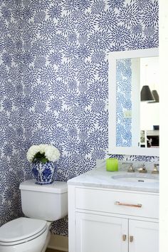 a white toilet sitting next to a bathroom sink under a blue and white wallpaper