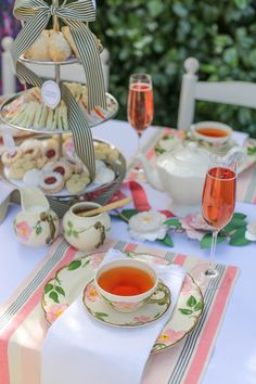 a table topped with tea cups and plates filled with desserts next to wine glasses