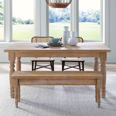 a wooden table with two chairs and a basket hanging from the ceiling over it, in front of large windows