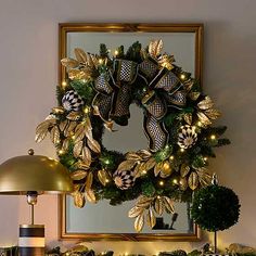 a christmas wreath on top of a mantle next to a lamp and other holiday decorations