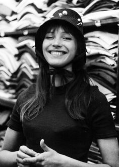 black and white photograph of a woman in front of stacks of shirts smiling at the camera