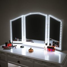 a vanity with three lighted mirrors and bottles on top of it in front of a mirror