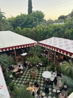 an aerial view of people sitting at tables in a garden with umbrellas and potted plants