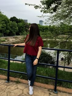 a woman leaning on a railing looking at the water and trees in the background,