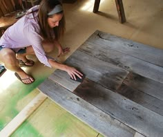 a woman kneeling down on the floor with her hand on top of a piece of wood