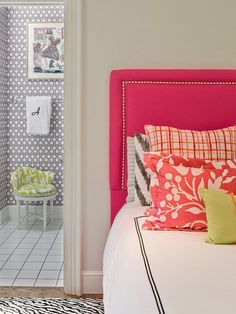 a pink headboard with colorful pillows on it in a white and black bedroom area