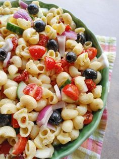 a green bowl filled with pasta salad on top of a checkered table cloth next to a fork