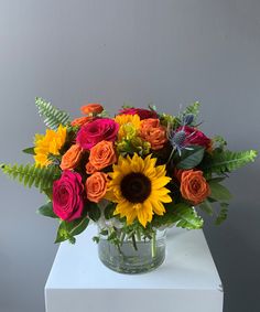 a vase filled with colorful flowers on top of a white table next to a gray wall