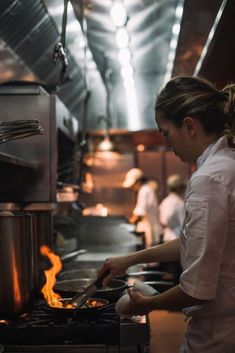 a woman cooking in a kitchen with flames coming out of the stove and pots on fire