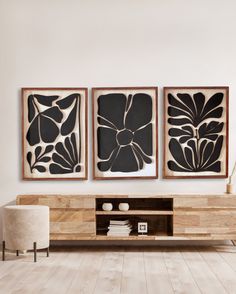 three black and white paintings hang on the wall above a wooden entertainment center in a modern living room