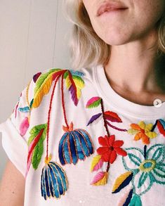 a woman with blonde hair wearing a white t - shirt with colorful flowers on it