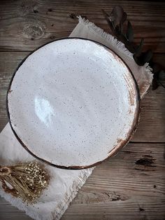 a white plate sitting on top of a wooden table next to dried flowers and leaves