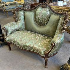 an ornate green couch sitting on top of a floor next to other chairs and tables