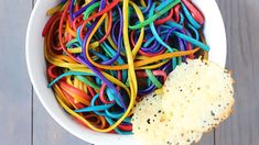 a white bowl filled with lots of different colored noodles and crackers next to a piece of bread