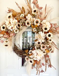 a wreath with flowers and feathers hanging on the front door