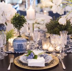 the table is set with blue and white dishes, silverware, candles, and flowers